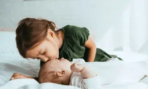 Starsza siostra czule całuje niemowlę w czoło. To uroczy obrazek, który może przypominać syndrom najstarszego dziecka, gdy przejmuje opiekę.