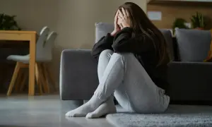 Kobieta siedzi na podłodze, zakrywając twarz dłońmi. Jej postawa sugeruje przygnębienie i objawy stresu długotrwałego.