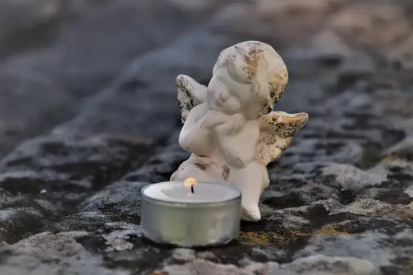 Aniołek czuwa przy płonącej świecy, symbolizując żałobę po rodzicach.